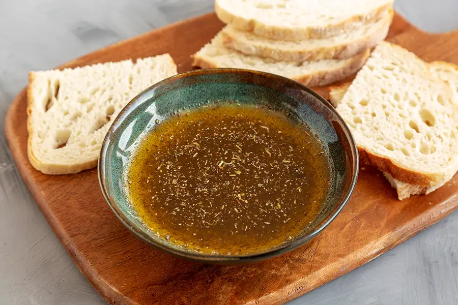 a stoneware bowl of Stevie's Italian Dressing & Marinade on a cutting board next to slices of crusty bread